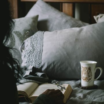 Woman reading book on bed with pillows and coffee on the side