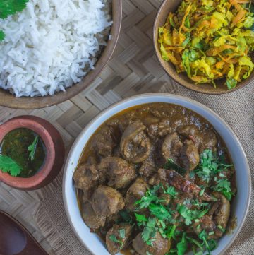 Indian style mutton kidney curry garnished with coriander leaves in white bowl along with rice and vegetables in other bowls