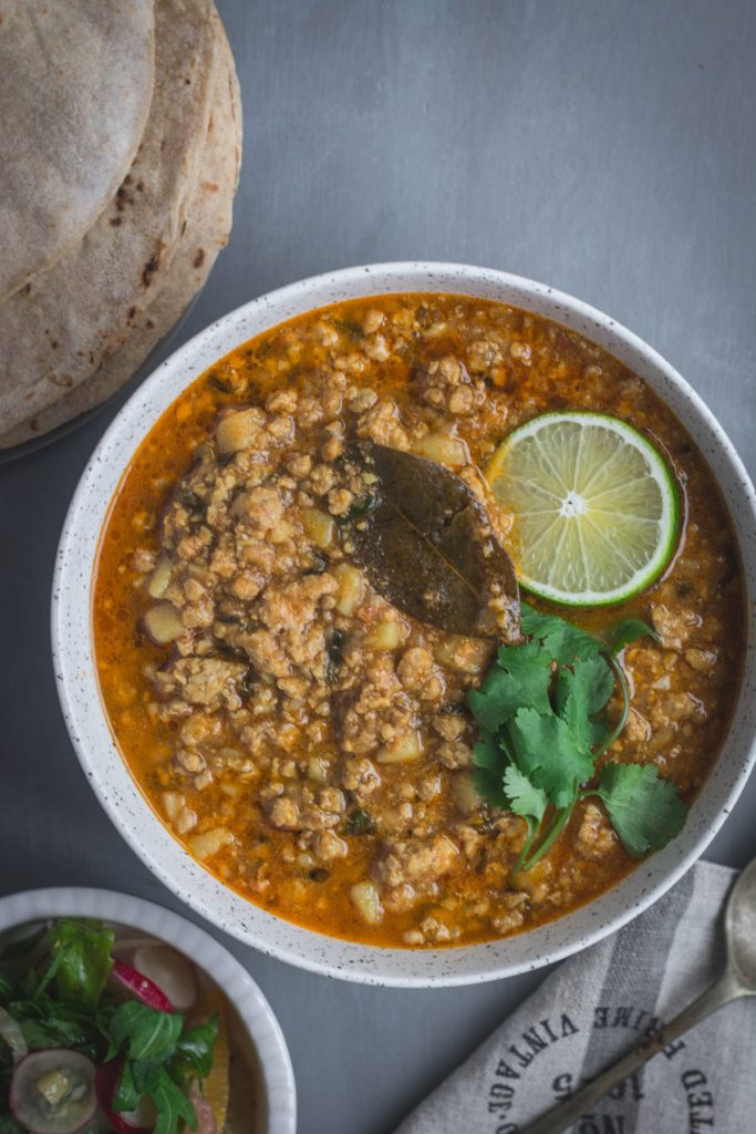 Indian pork mince curry garnish with lime and coriander leaves in grey bowl