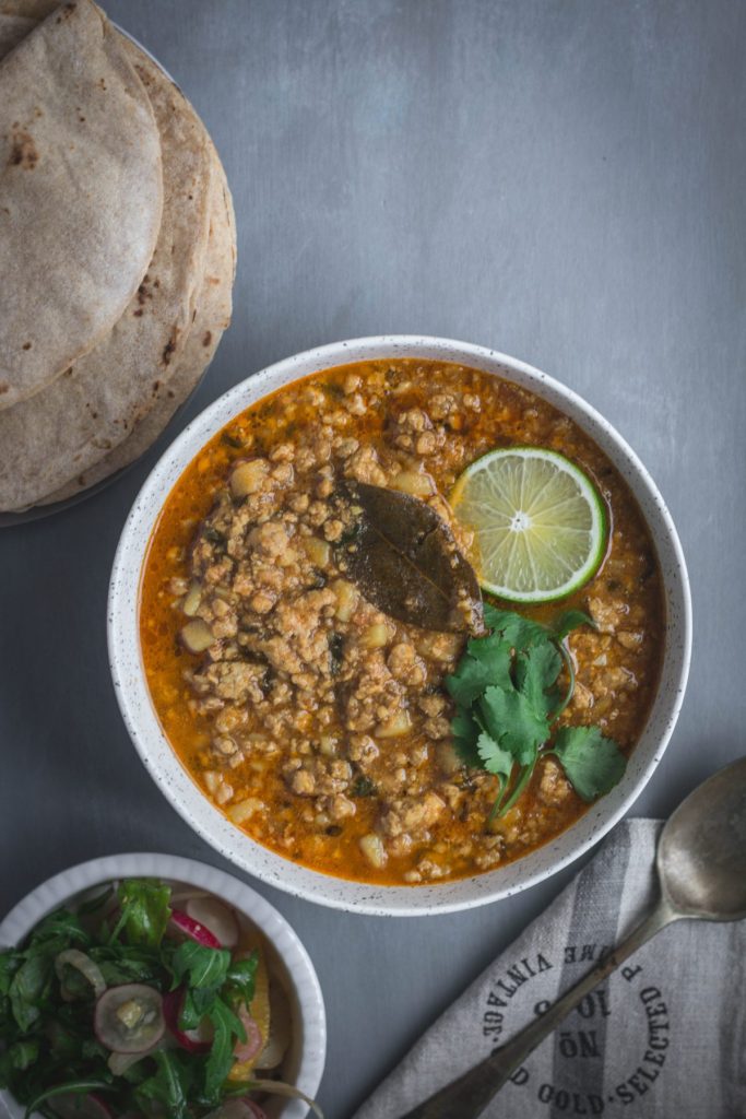 Indian pork mince curry garnished with lime and coriander leaves in grey bowl