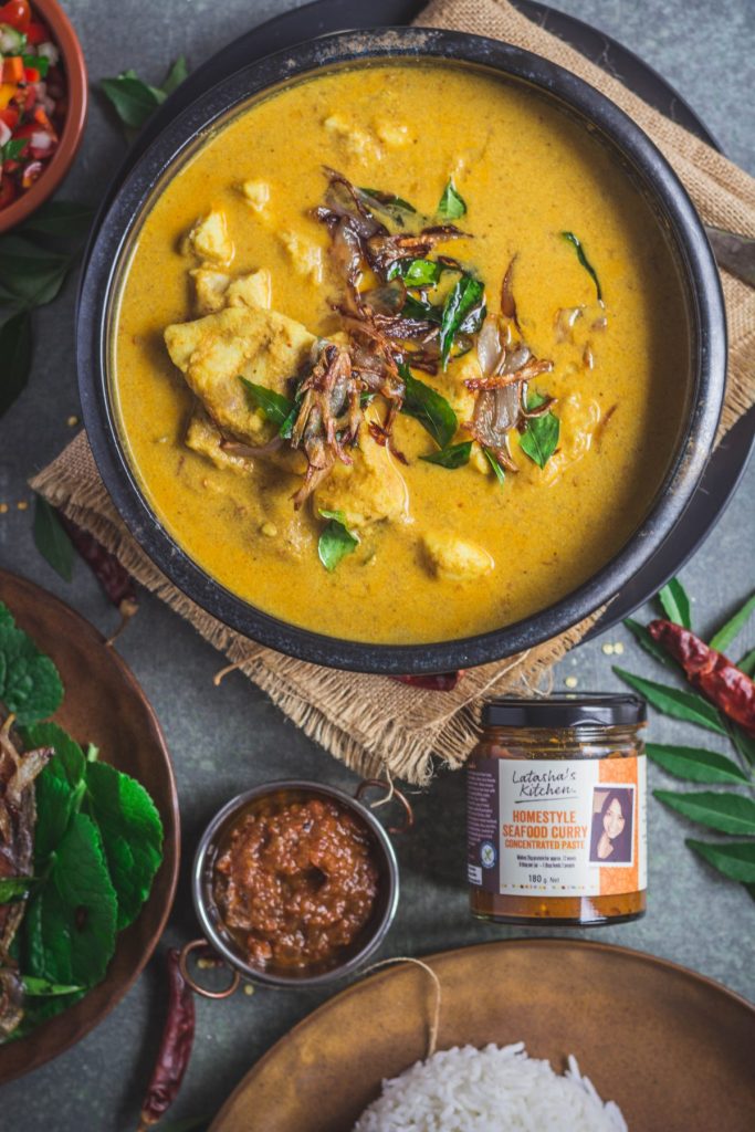 Indian style fish curry in black bowl with a bottle of seafood curry paste on the side