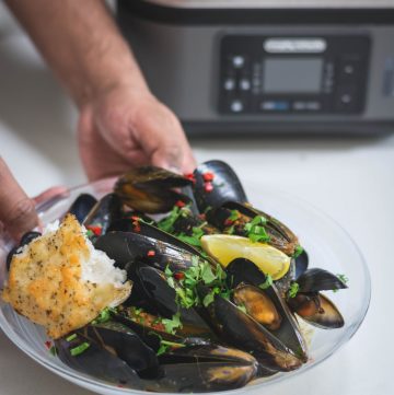 hand holding white bowl with steamed mussels and garlic bread