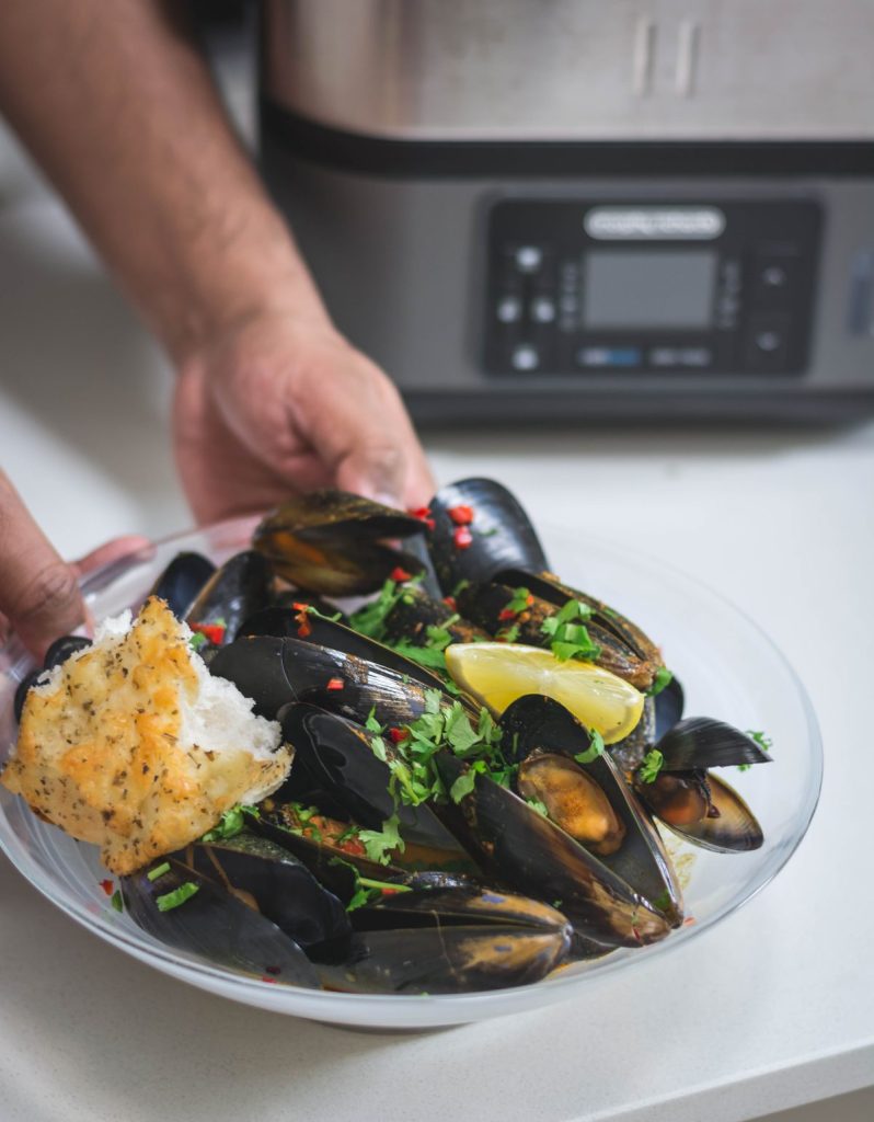 hand holding white bowl with steamed mussels and garlic bread