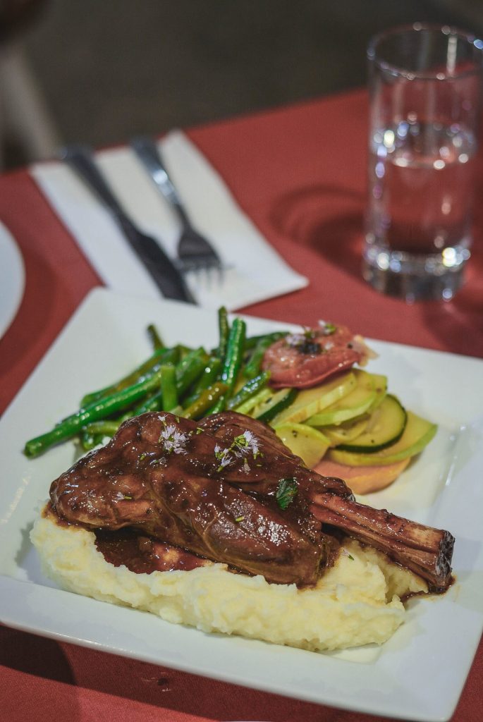 Lamb shanks slow cooked with wine and rosemary with mashed potato and roasted vegetables on white plate