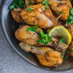 Baked chicken drumsticks with a slice of lemon on top in a black plate