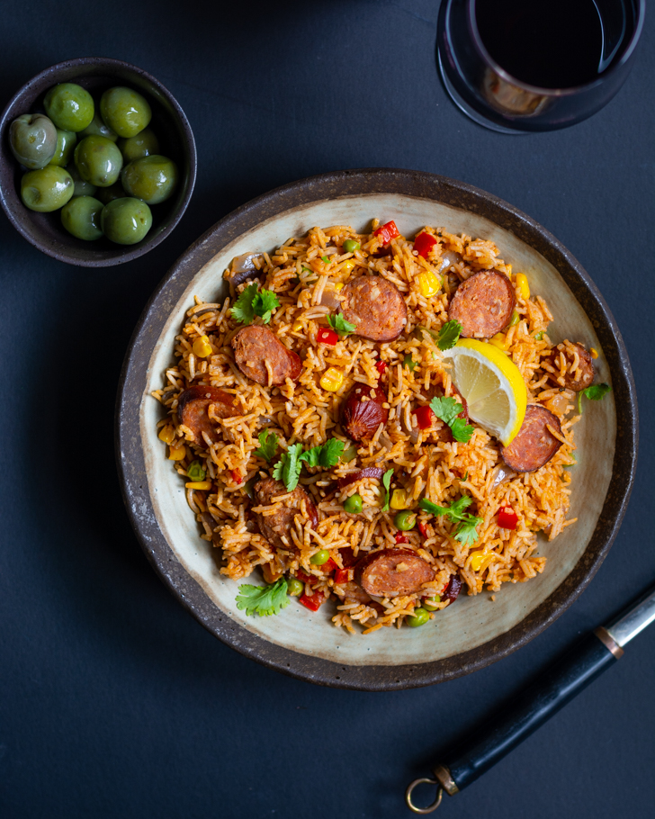 Spanish rice with chorizo in grey bowl with green olives on the side