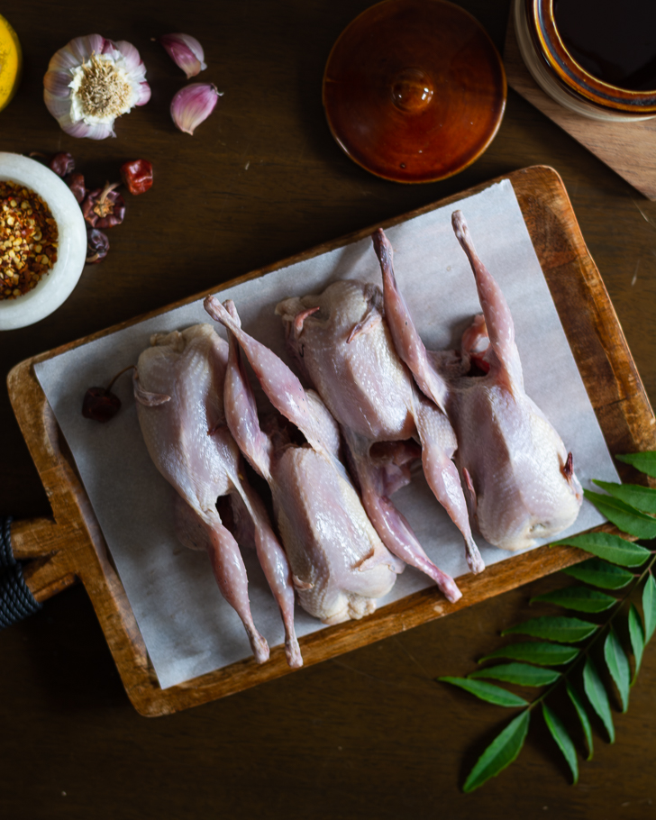four raw quail meat on a wooden platter with spices on the side
