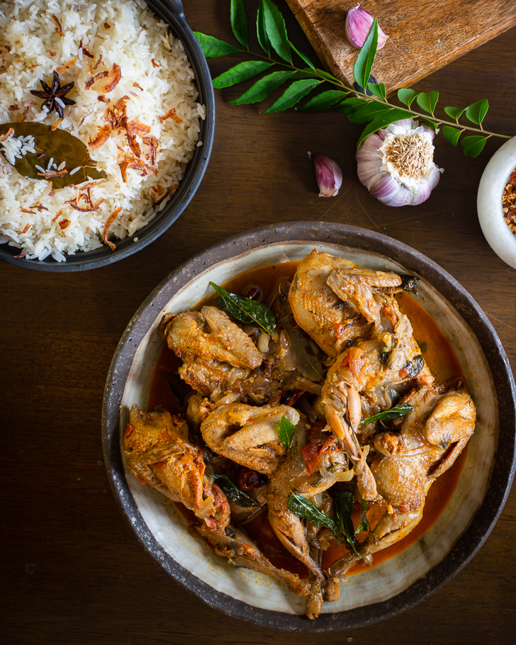 Quail curry served in grey bowl with rice, chilli and garlic in the background