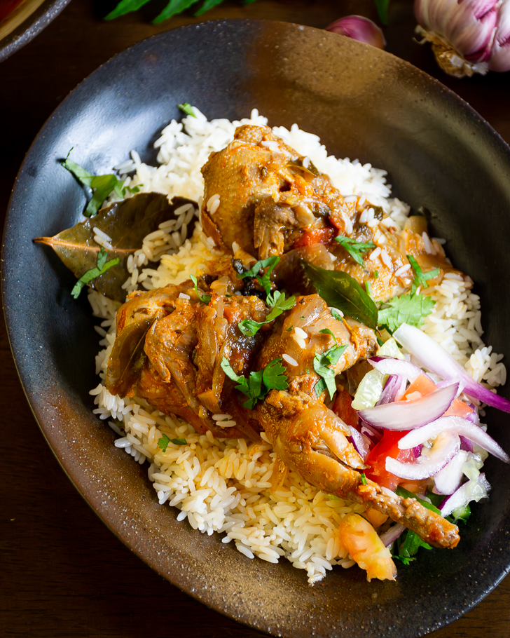 Two pieces of quail curry served on a bed of rice and salad